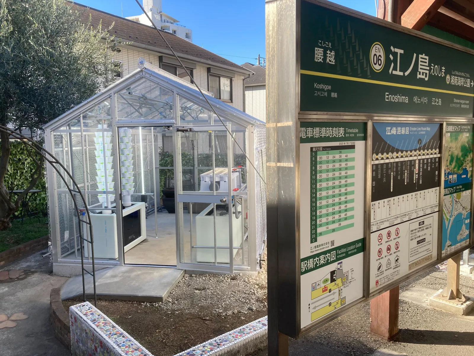 A small glass greenhouse beside the Enoshima Station platform sign