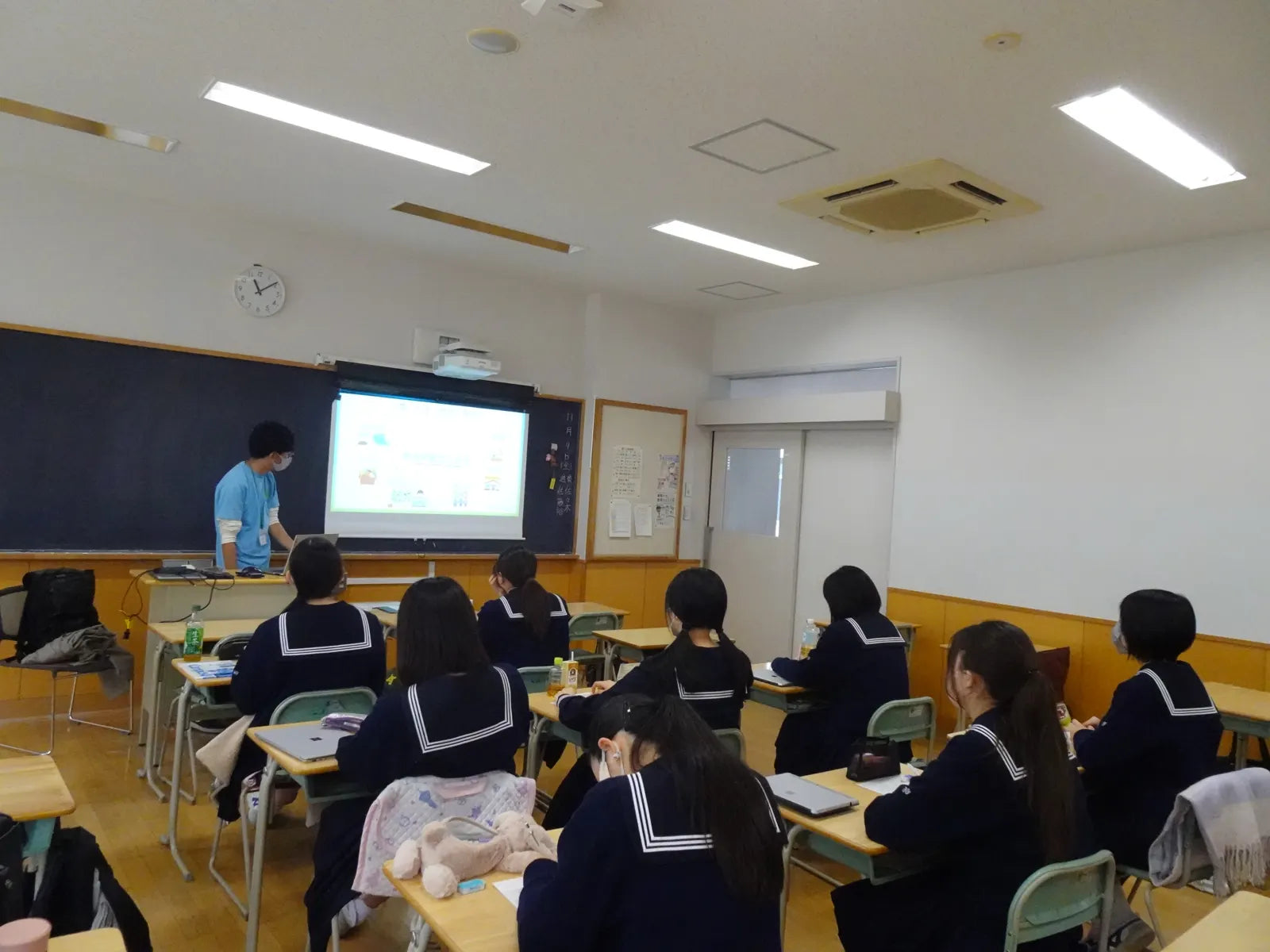 A classroom seen from the back, students facing a presentation on aquaponics