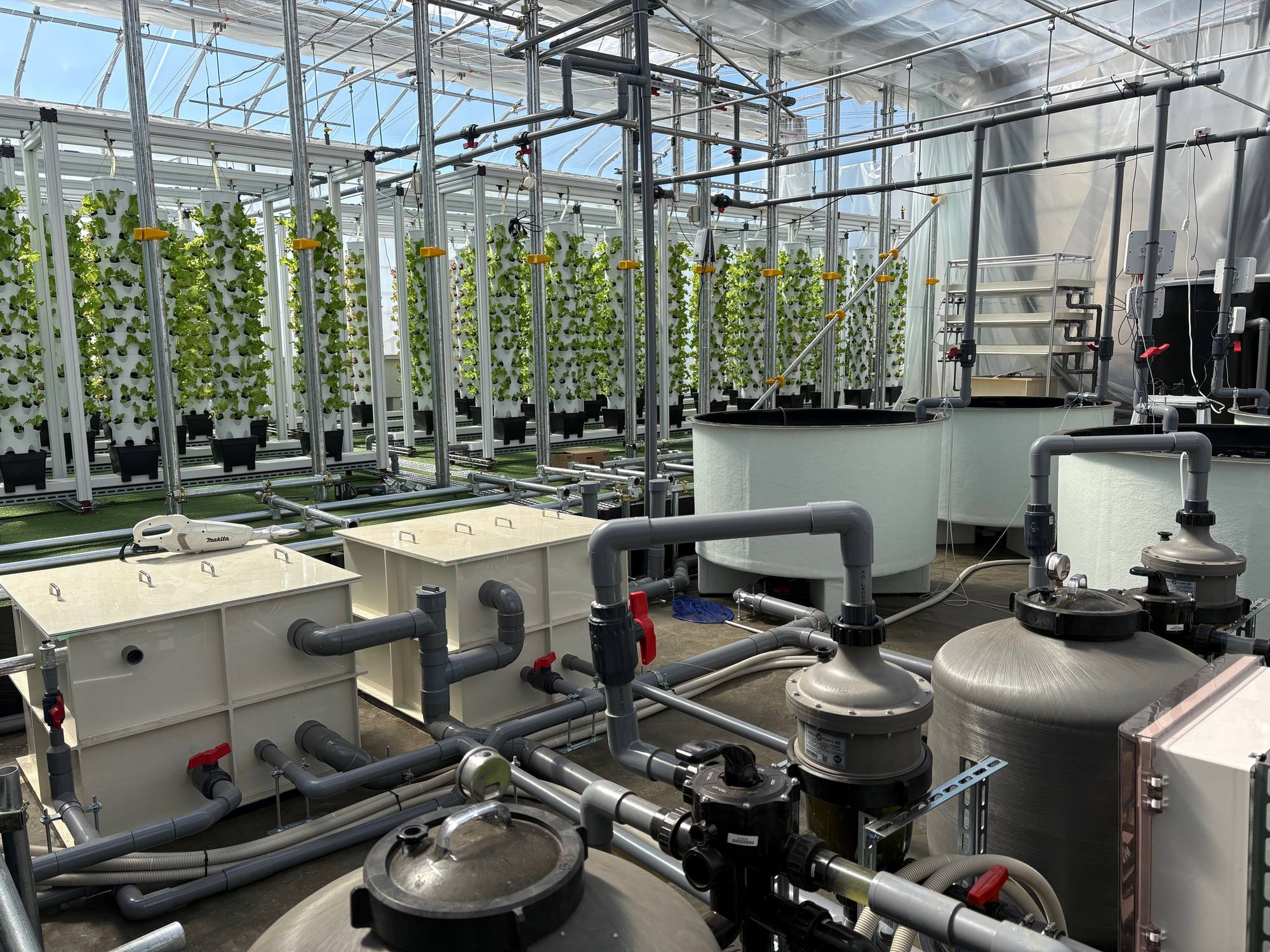 Filtration tanks and pipework in front of rows of vertical grow towers under glass