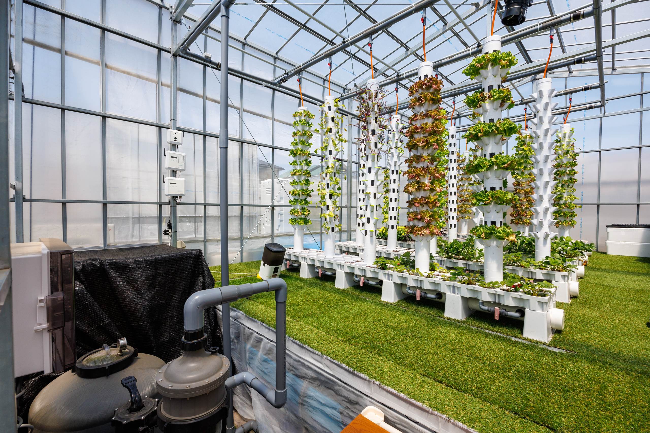 Vertical grow towers over planted beds, with filtration and pipework in the foreground